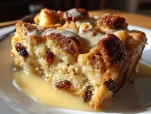 A close-up of a slice of old-fashioned bread pudding, studded with raisins and drizzled with a creamy sauce.