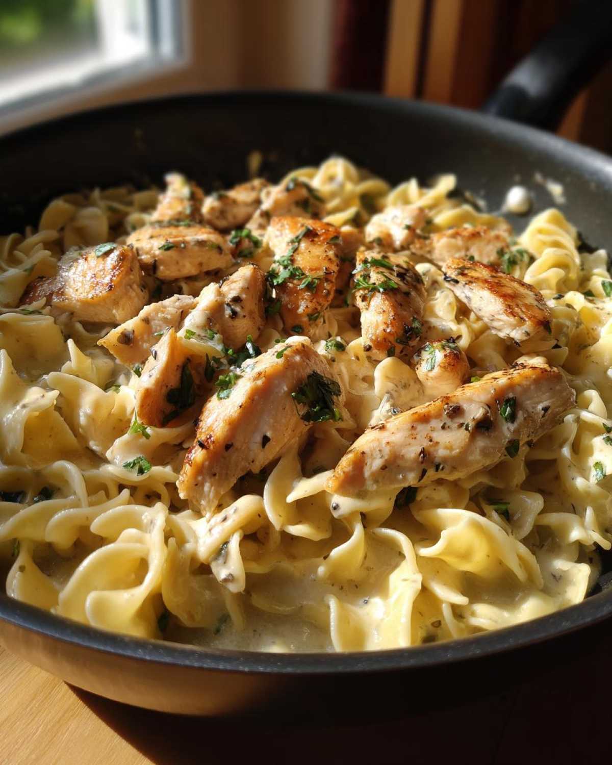 Close-up of a skillet filled with one-pan chicken and buttered noodles, garnished with parsley.