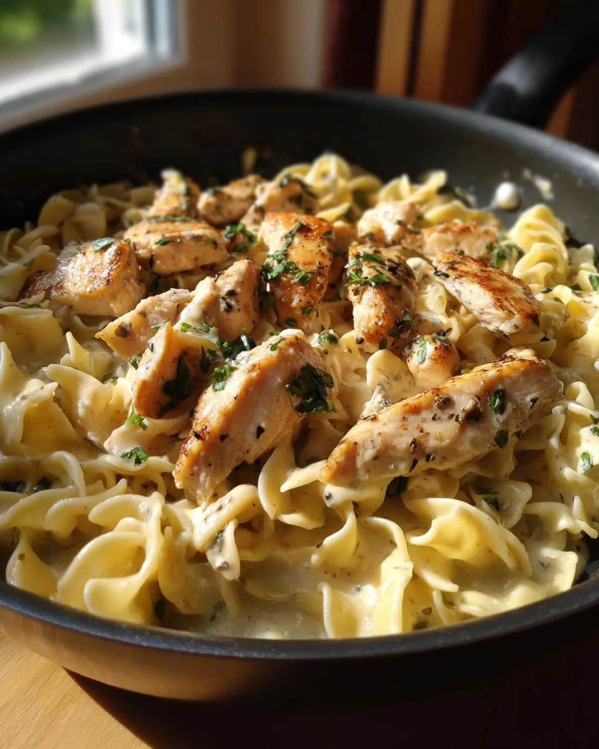 Close-up of a skillet filled with one-pan chicken and buttered noodles, garnished with parsley.