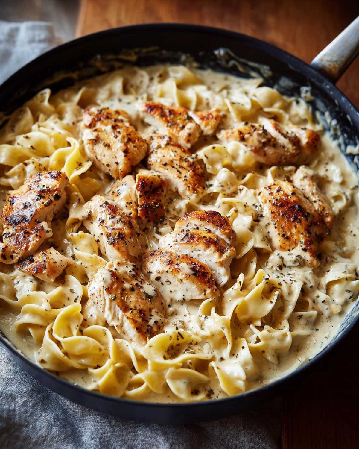Close-up of one-pan chicken and buttered noodles in a creamy sauce, garnished with herbs.