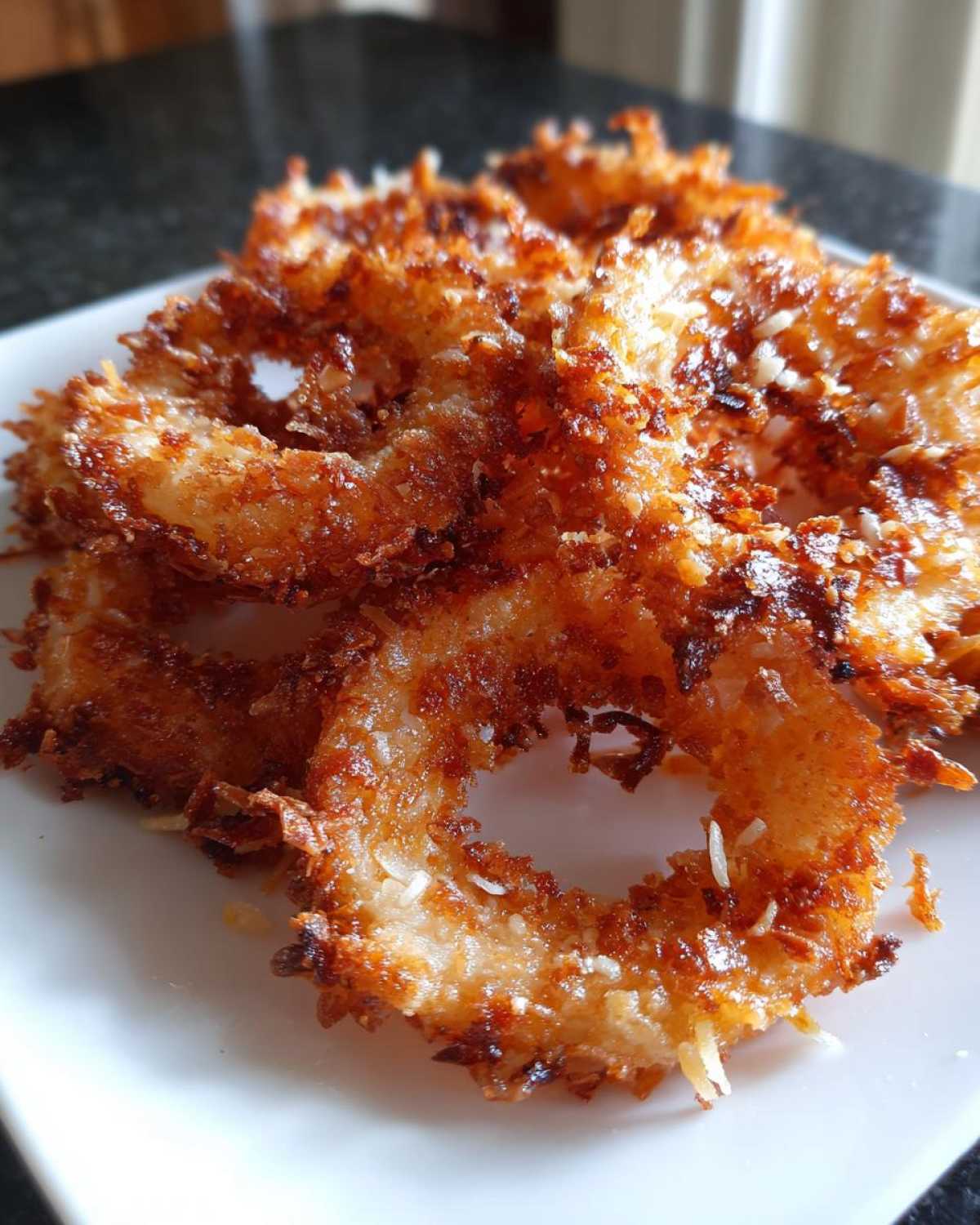 Close-up of golden-brown, crispy parmesan onion rings on a white plate.
