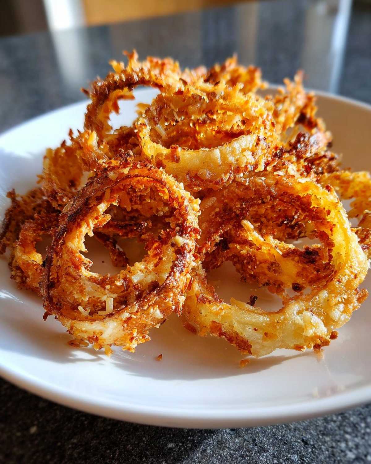 A close-up of a pile of golden brown parmesan onion crisps on a white plate.