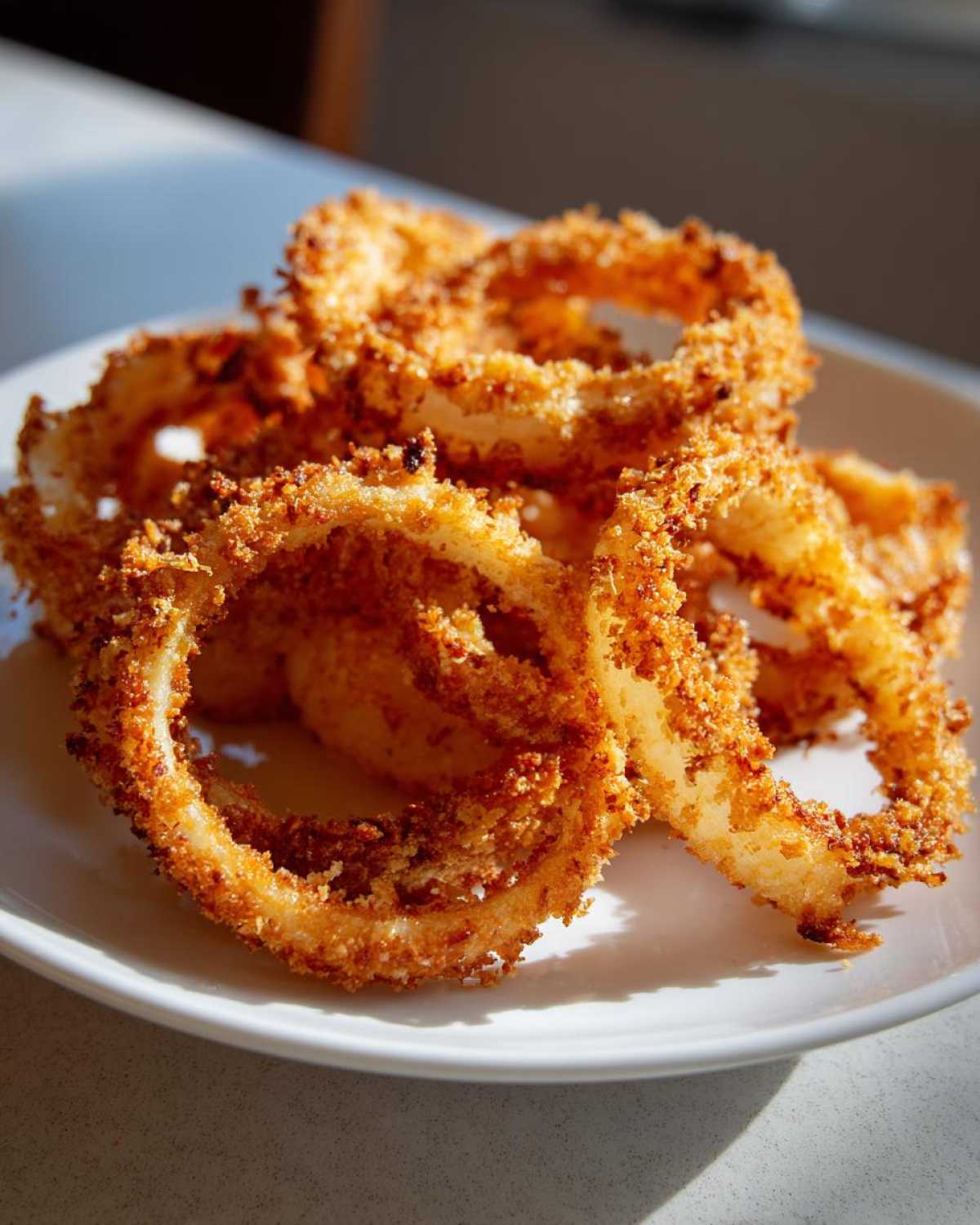 A close-up of golden-brown parmesan onion crisps piled on a white plate, ready to be enjoyed.