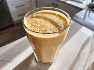 A tall glass filled with a thick, frothy peanut butter banana smoothie sitting on a bright countertop.