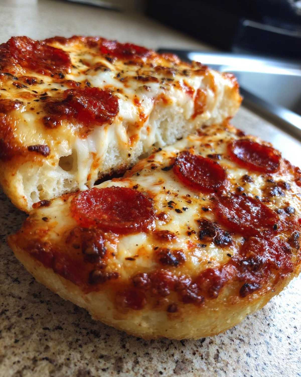 Two halves of a freshly baked pepperoni english muffin pizza showing melted cheese and a thick base.