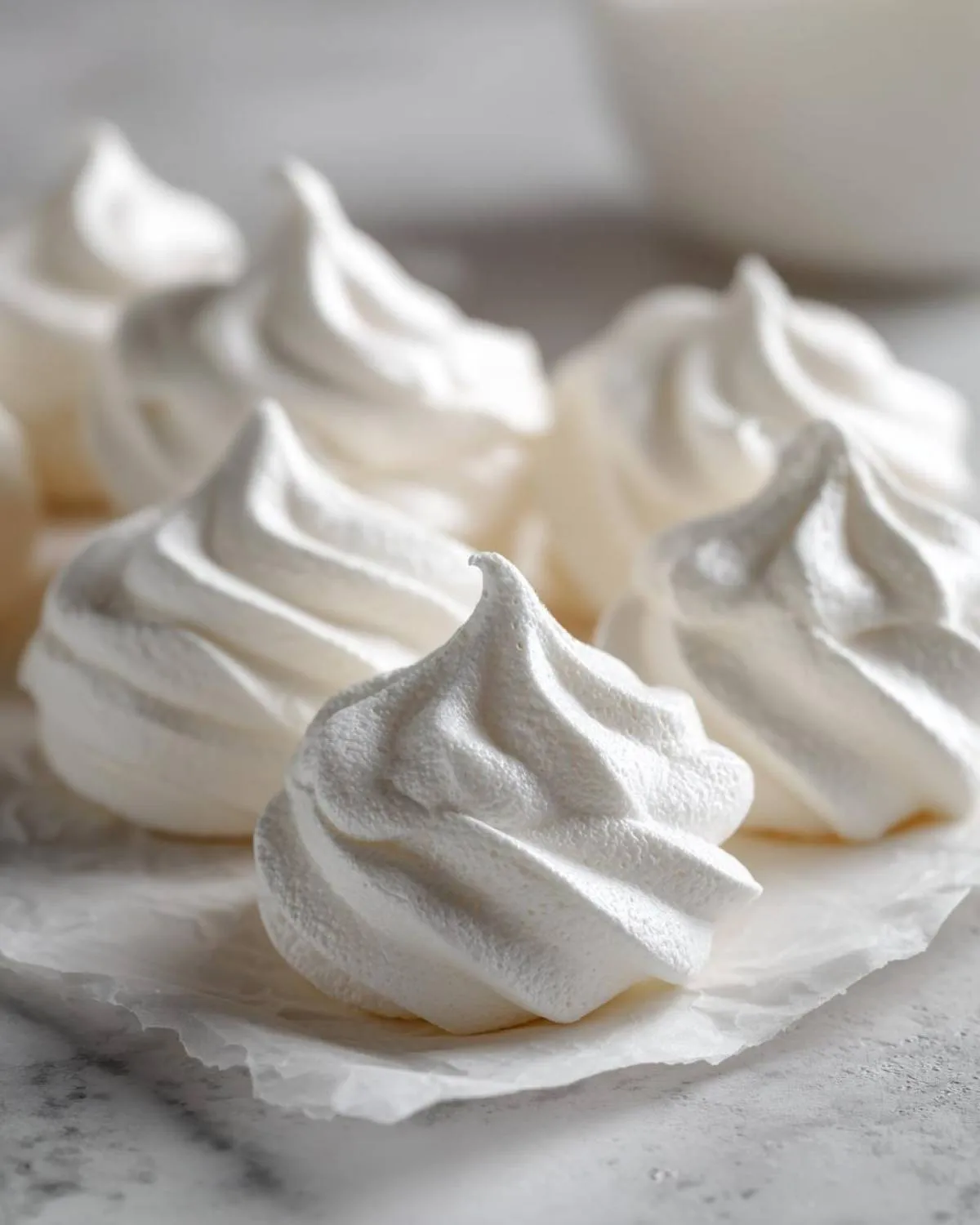 Close-up of several perfectly piped, crisp white meringue cookies resting on parchment paper.