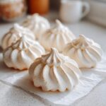 Close-up of several perfectly piped, white meringue cookies resting on parchment paper.