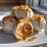 Close-up of white chocolate covered pumpkin cheesecake truffles topped with crumble and drizzled with white chocolate.
