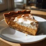 A delicious slice of creamy pumpkin mascarpone pie, topped with whipped cream and cinnamon, on a white plate.