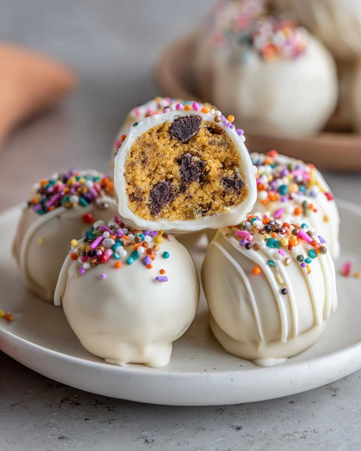 Close-up of Pumpkin Oreo Balls dipped in white chocolate, topped with colorful sprinkles and chocolate chips inside.