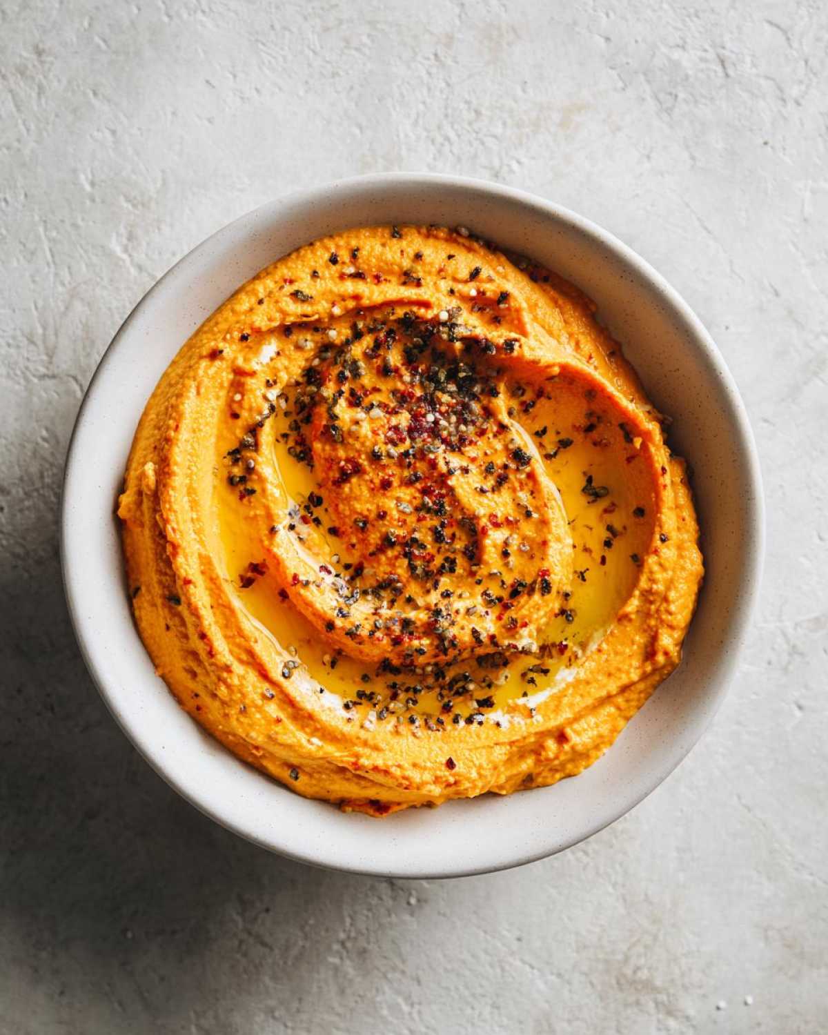 A bowl of creamy Pumpkin Whipped Feta Dip, drizzled with olive oil and topped with red pepper flakes and black pepper.