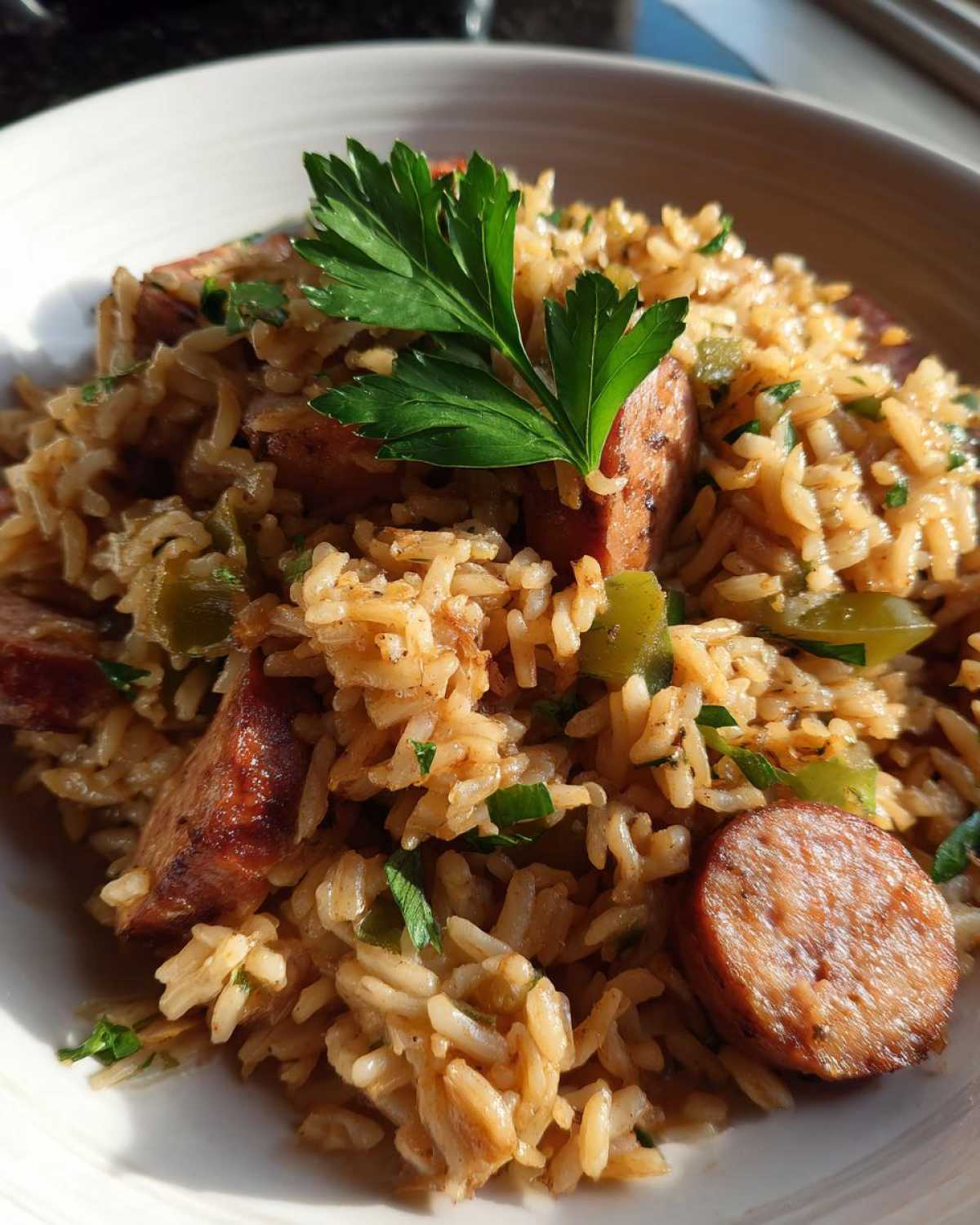 Close-up of a bowl of seasoned sausage and rice mixed with green peppers and topped with fresh parsley.