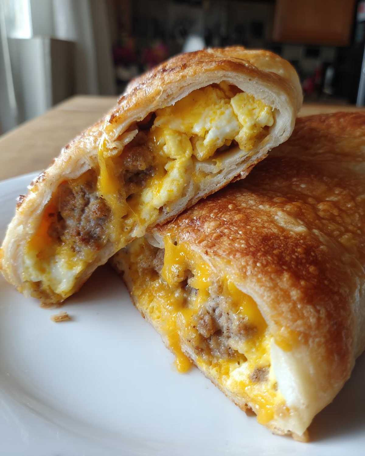 Close-up of a sausage egg breakfast roll up cut in half, showing fluffy scrambled eggs, savory sausage, and melted cheddar cheese.