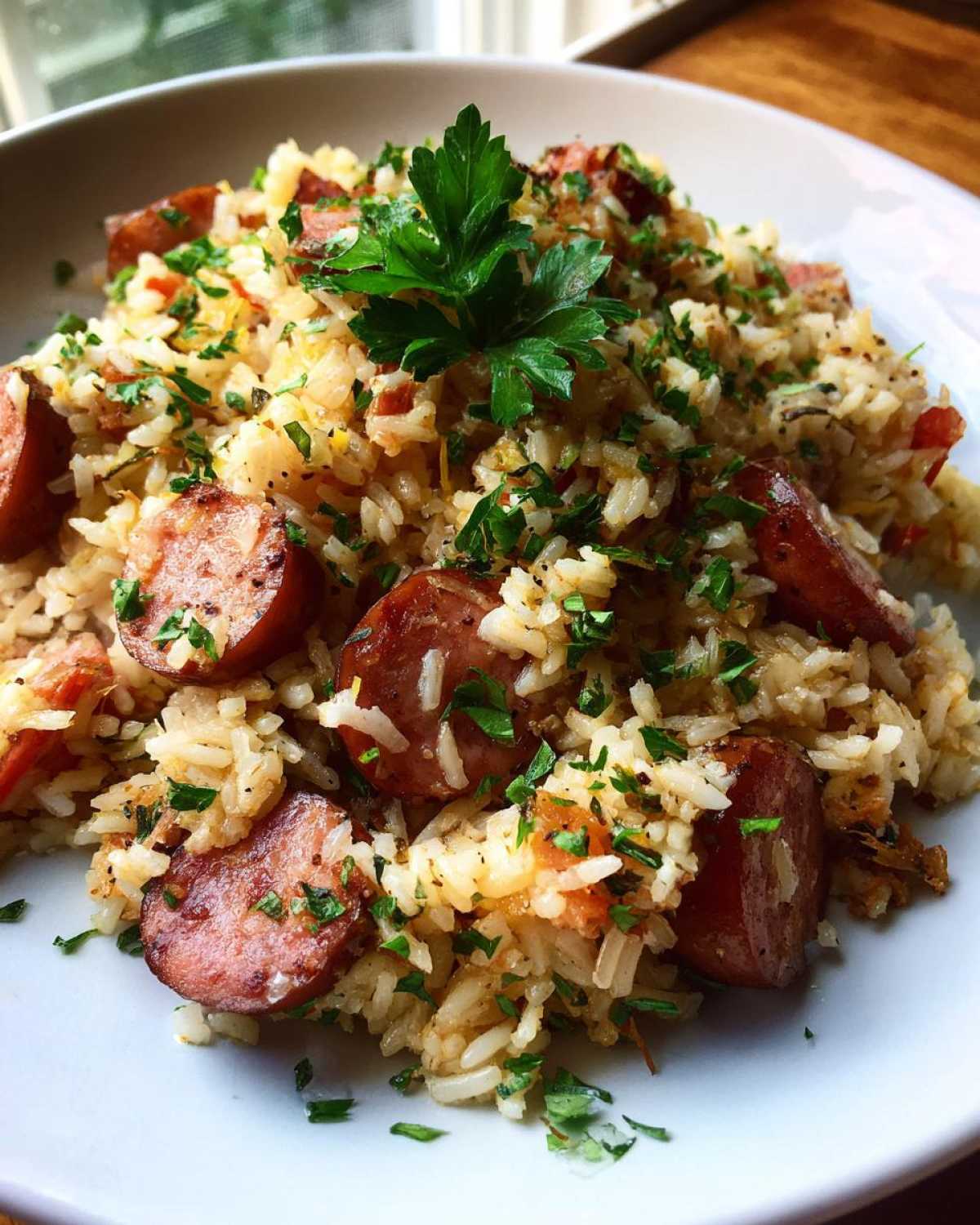 Close-up of savory sausage and rice mixed together, topped with fresh chopped parsley.