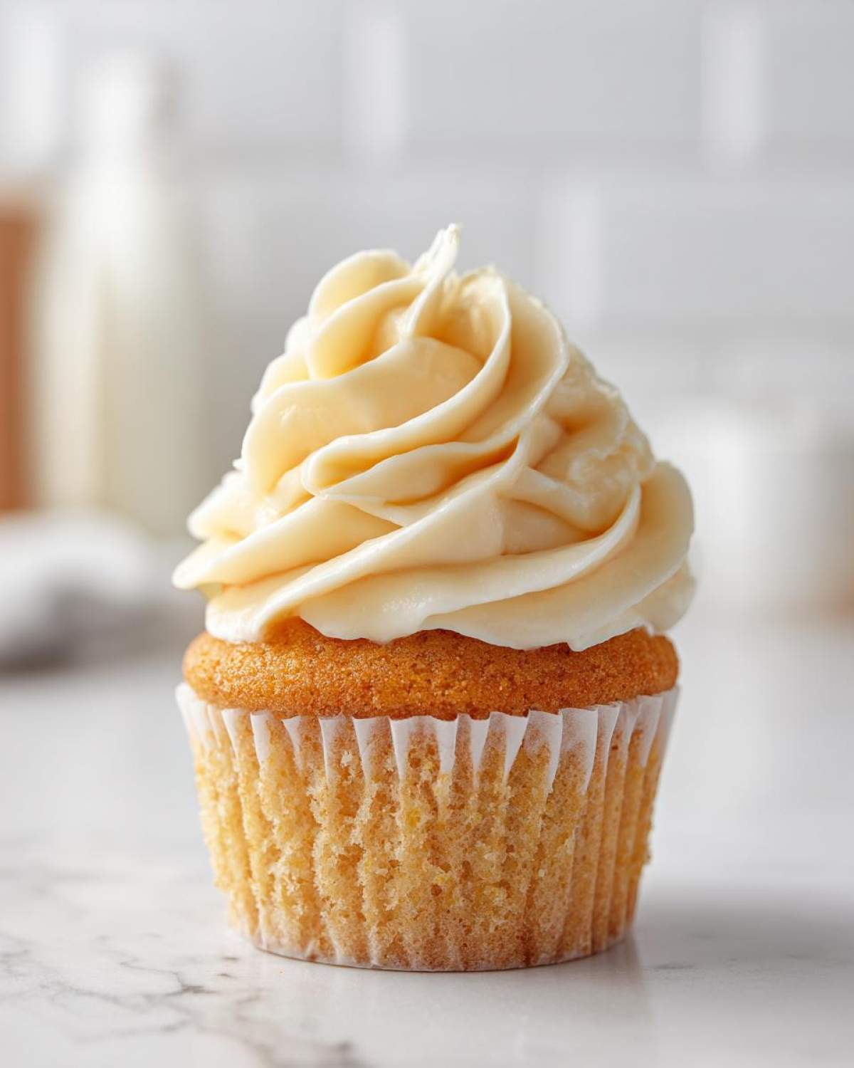 A single, beautifully frosted vanilla cupcake with creamy yellow buttercream on a white marble surface.