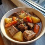 A steaming bowl of slow cooker beef stew, featuring tender chunks of beef, carrots, and potatoes, garnished with parsley.