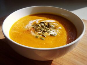 A bowl of creamy slow cooker pumpkin soup topped with pumpkin seeds and a swirl of cream.