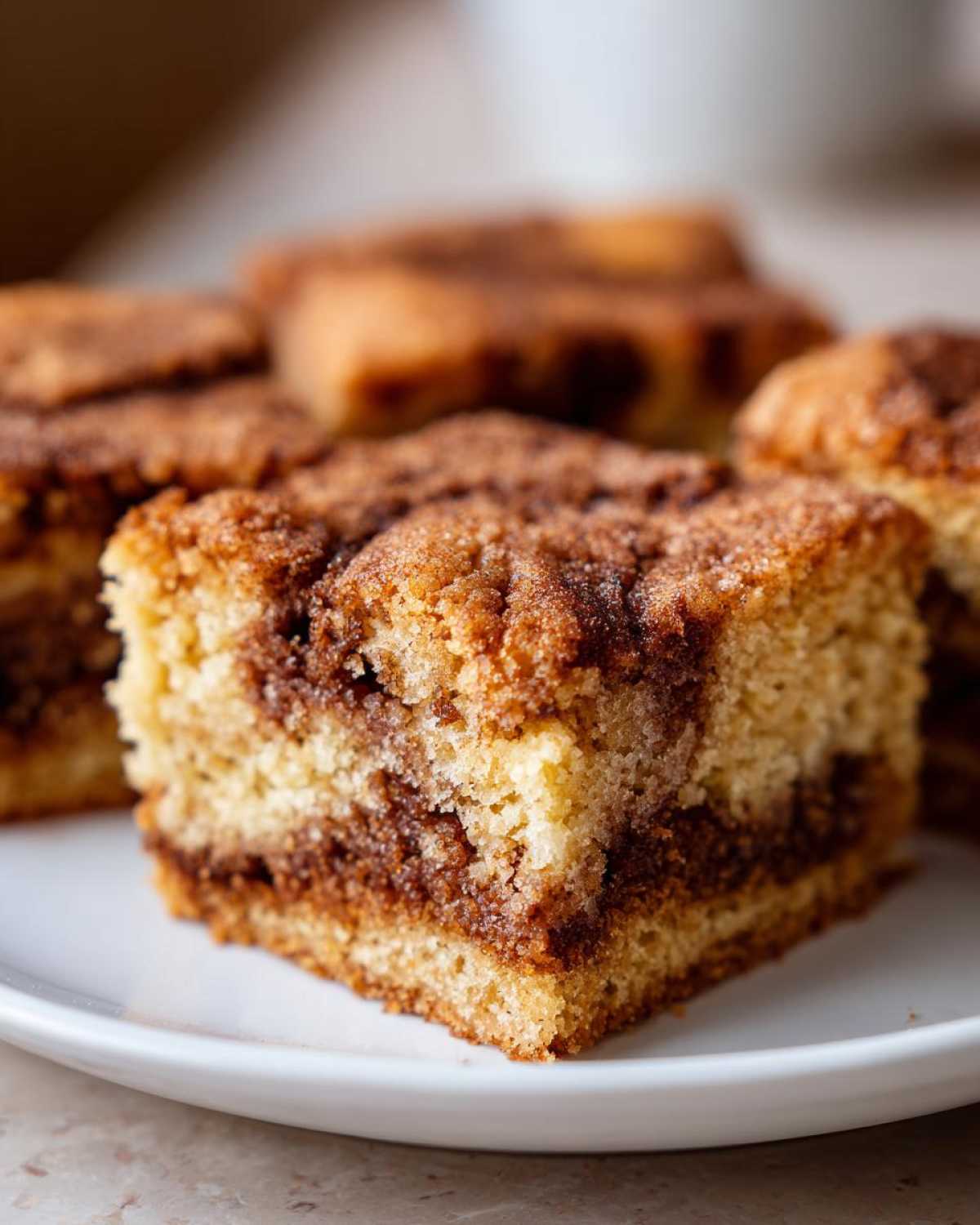 A close-up of a square snickerdoodle blondies slice showing a rich cinnamon swirl texture on a white plate.