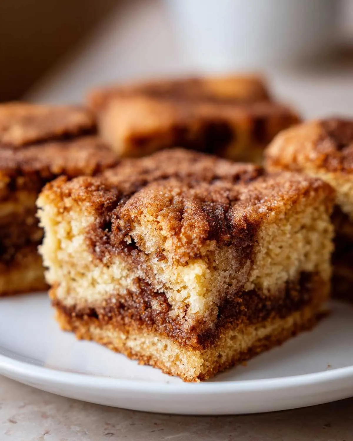 A close-up of a square snickerdoodle blondies slice showing a rich cinnamon swirl texture on a white plate.