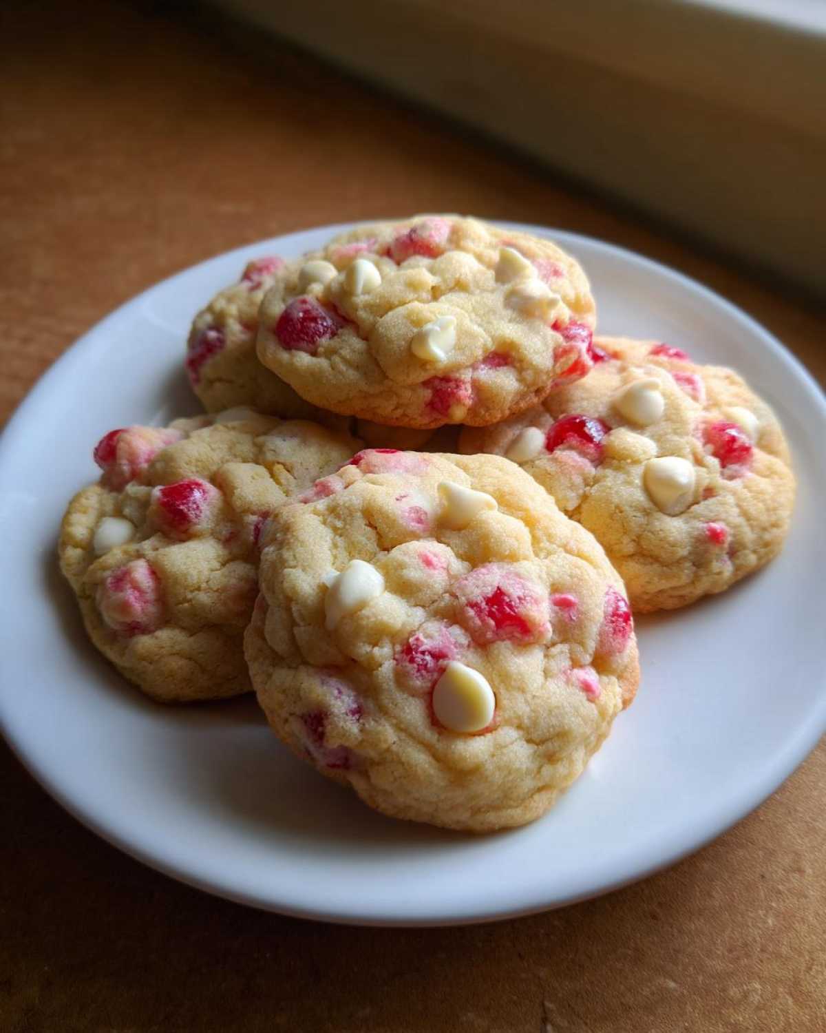A pile of soft cherry chip cookies with white chocolate chips on a white plate.
