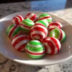 A pile of shiny, round Soft Christmas peppermints with red and green stripes in a white bowl.