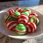 A pile of shiny, round Soft Christmas peppermints with red and green stripes in a white bowl.