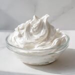 A clear glass bowl filled with perfectly stiff, bright white royal icing recipe mixture.