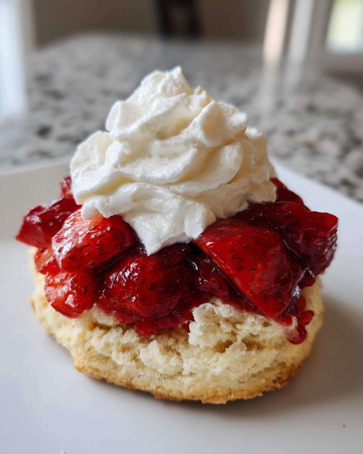 A single serving of classic strawberry shortcake featuring a biscuit base, macerated strawberries, and whipped cream.