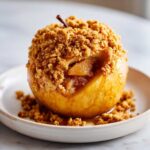 Close-up of a golden baked apple topped generously with a brown sugar and oat crumble filling.