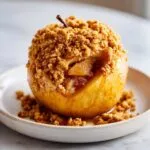 Close-up of a golden baked apple topped generously with a brown sugar and oat crumble filling.