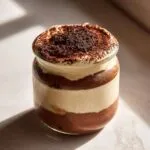 A layered tiramisu chia pudding in a glass jar, topped with cocoa powder.