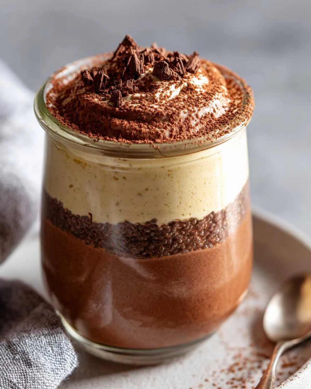 A layered tiramisu chia pudding in a glass jar, topped with cream and chocolate shavings.