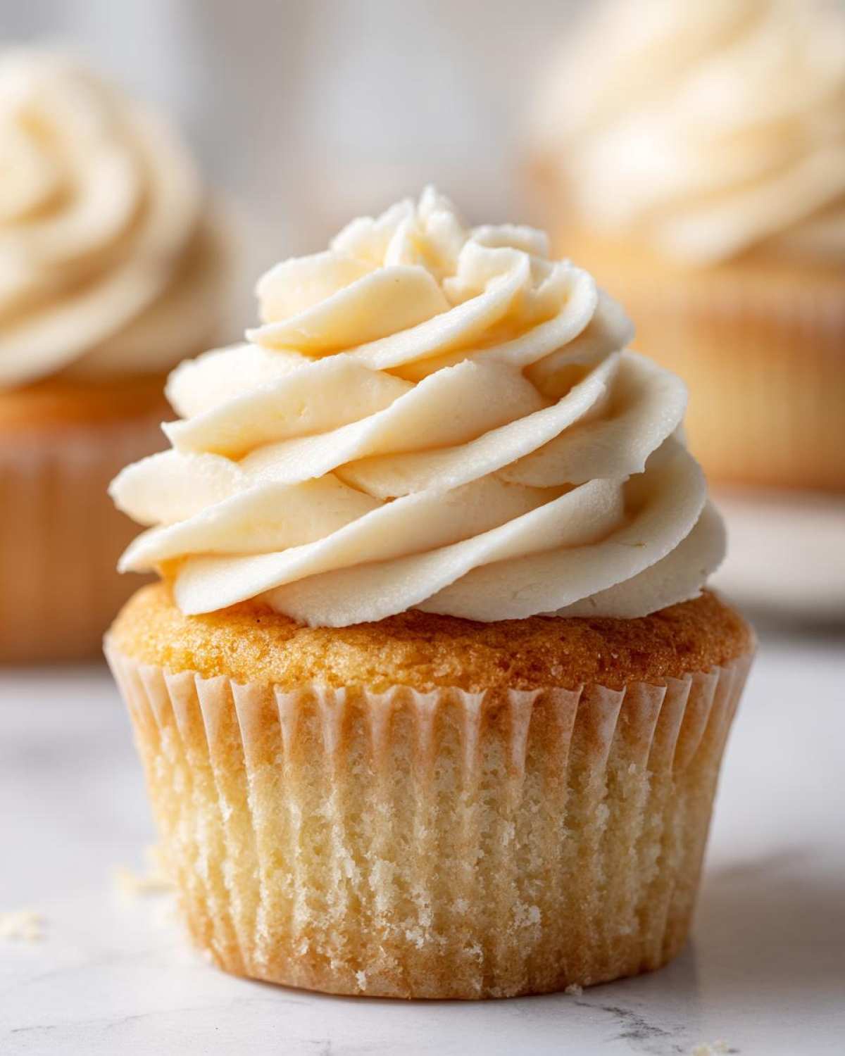 A close-up shot of a single, freshly baked vanilla cupcake topped with a swirl of creamy vanilla frosting.
