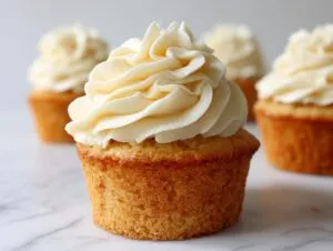 A close-up of a perfectly baked vanilla cupcake topped with rich, swirled vanilla buttercream frosting.