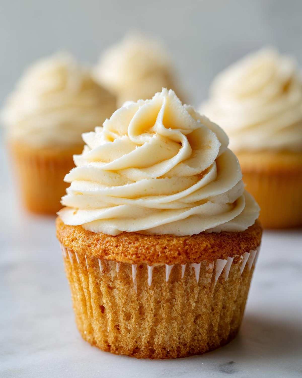 Close-up of a single, perfectly baked vanilla cupcake with tall swirl of creamy white frosting.