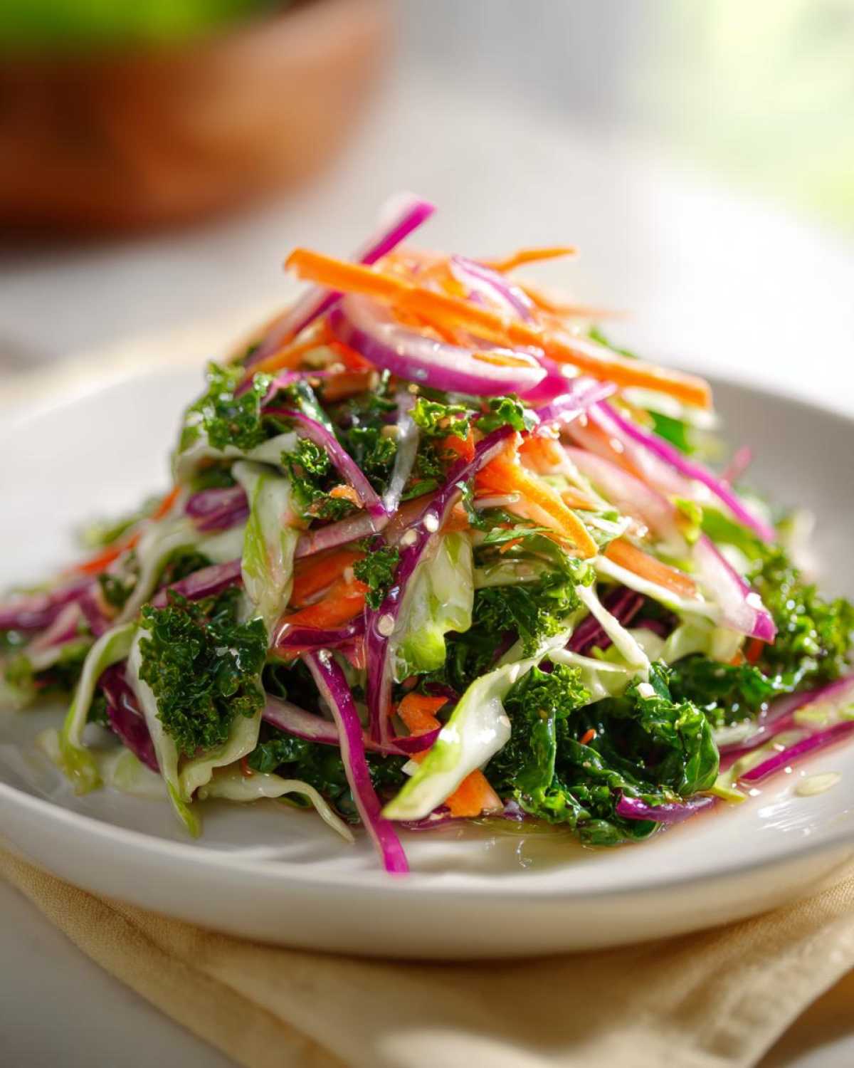 A vibrant, fresh cabbage salad featuring kale, shredded carrots, and red onion slices, lightly dressed.