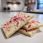 Close-up of three pieces of white chocolate candy cane bark, topped with crushed candy canes.