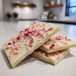 Close-up of three pieces of white chocolate candy cane bark, topped with crushed candy canes.