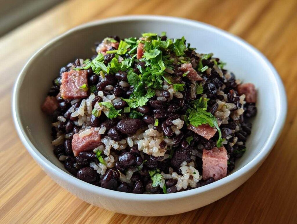 A close-up of a white bowl filled with flavorful black beans and rice mixed with chunks of ham and topped with fresh cilantro.