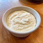 Close-up of creamy, white homemade garlic sauce with visible minced garlic pieces in a small white bowl.