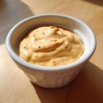 Creamy, orange-hued burger sauce speckled with red pepper flakes in a small white bowl.