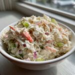 A close-up of creamy crab salad mixed with celery and red onion in a white bowl.