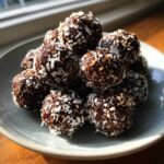 A close-up of a mound of dark, rich coconut balls generously rolled in shredded coconut flakes.