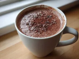 Close-up of a steaming mug of rich hot chocolate topped with cocoa powder and chocolate shavings.