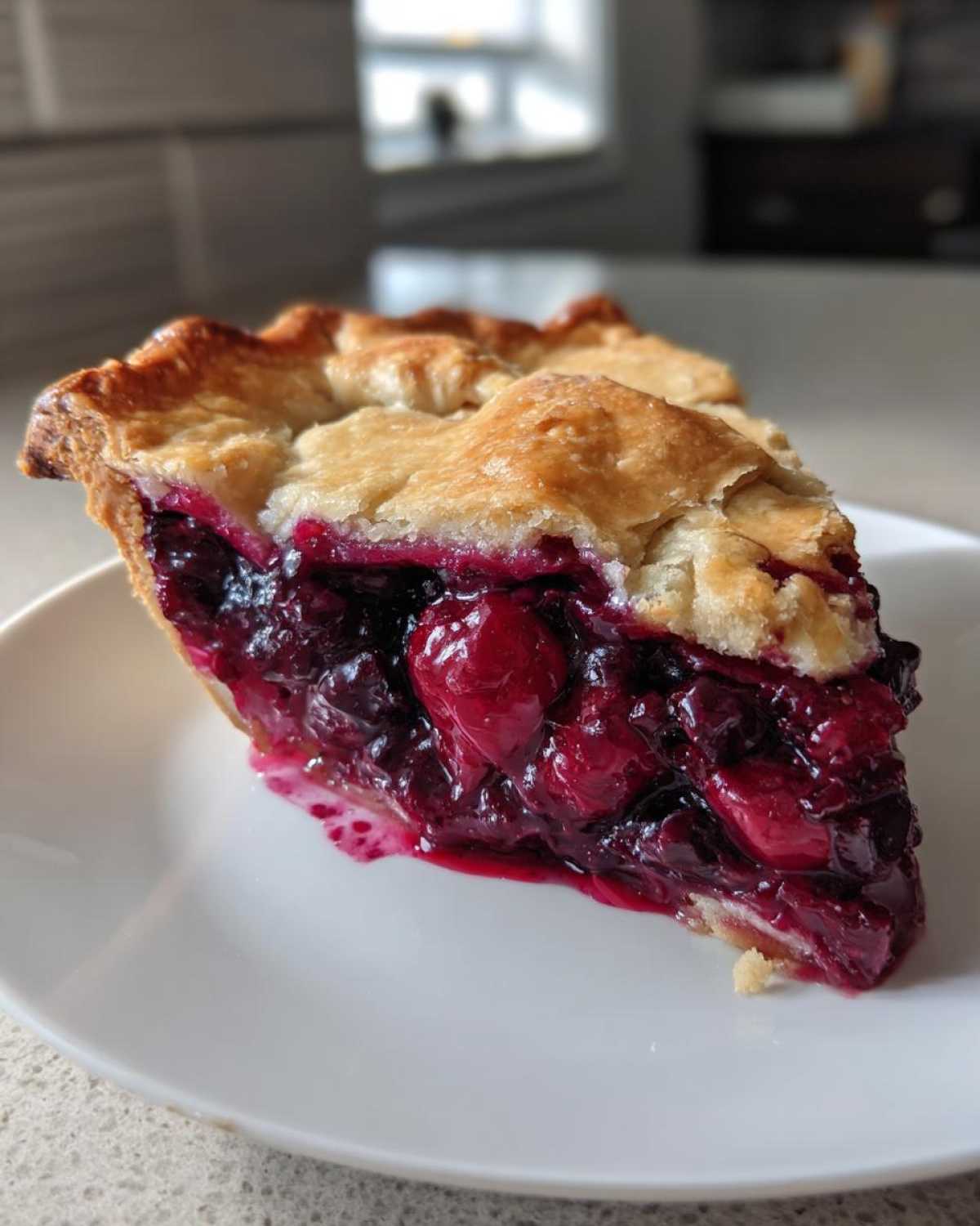 A close-up of a thick slice of berry pie showing juicy, dark red filling and a flaky golden crust.