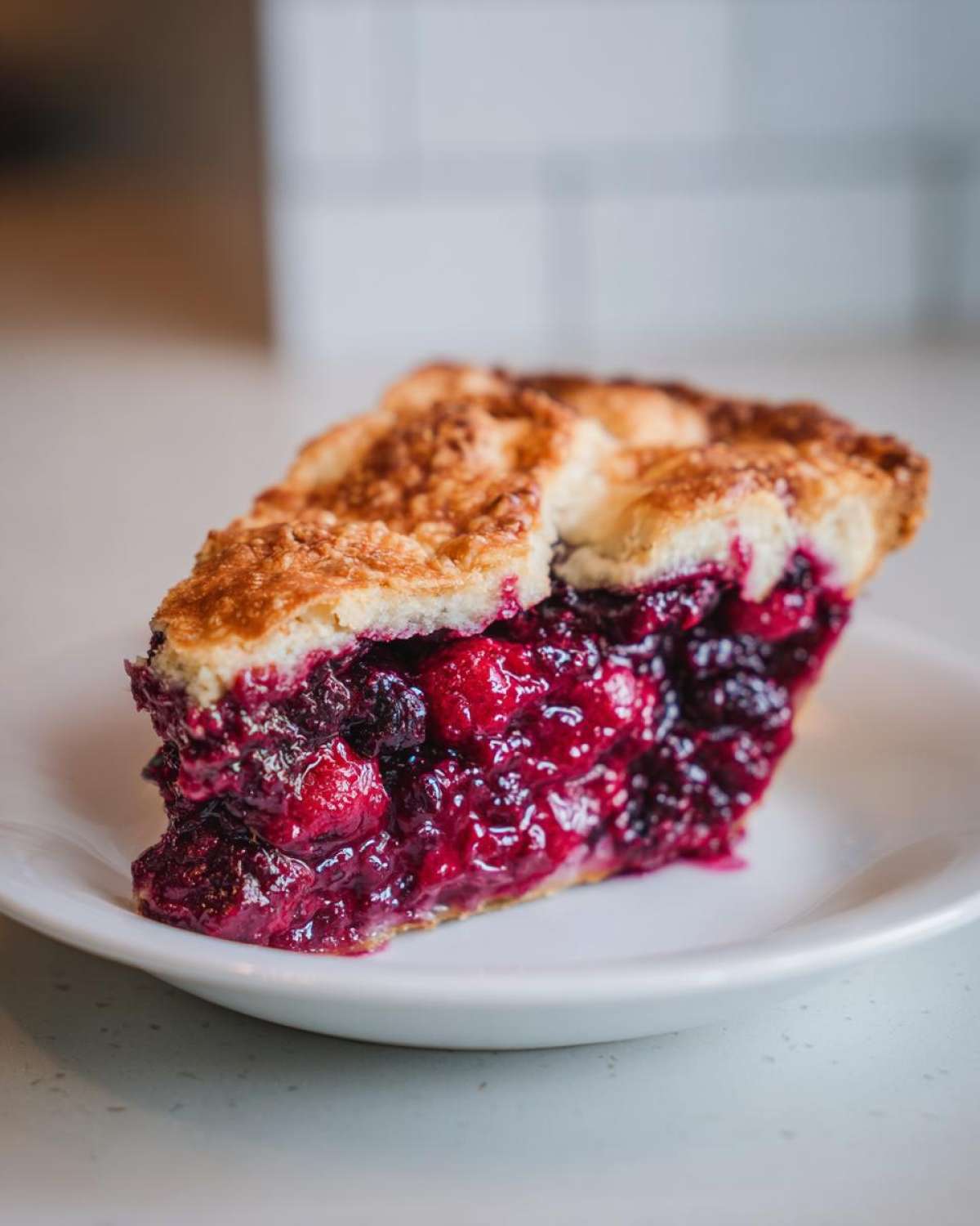 Close-up of a thick slice of amazing berry pie showing a golden, flaky crust and a rich, deep red berry filling.