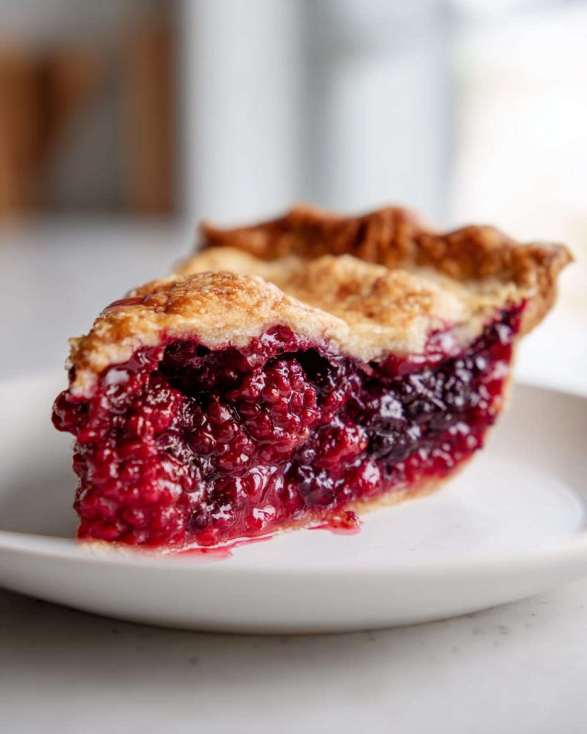 Close-up of a perfect slice of berry pie showing a thick, vibrant red filling and golden crust.