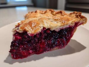 Close-up of a thick slice of amazing berry pie showing a rich, dark purple filling and flaky, golden-brown crust.