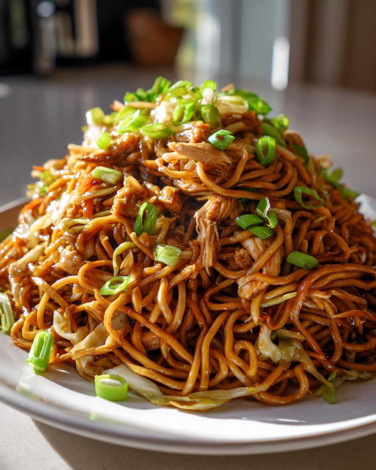 A large mound of glossy, saucy chicken chow mein recipe noodles topped with fresh green onions.