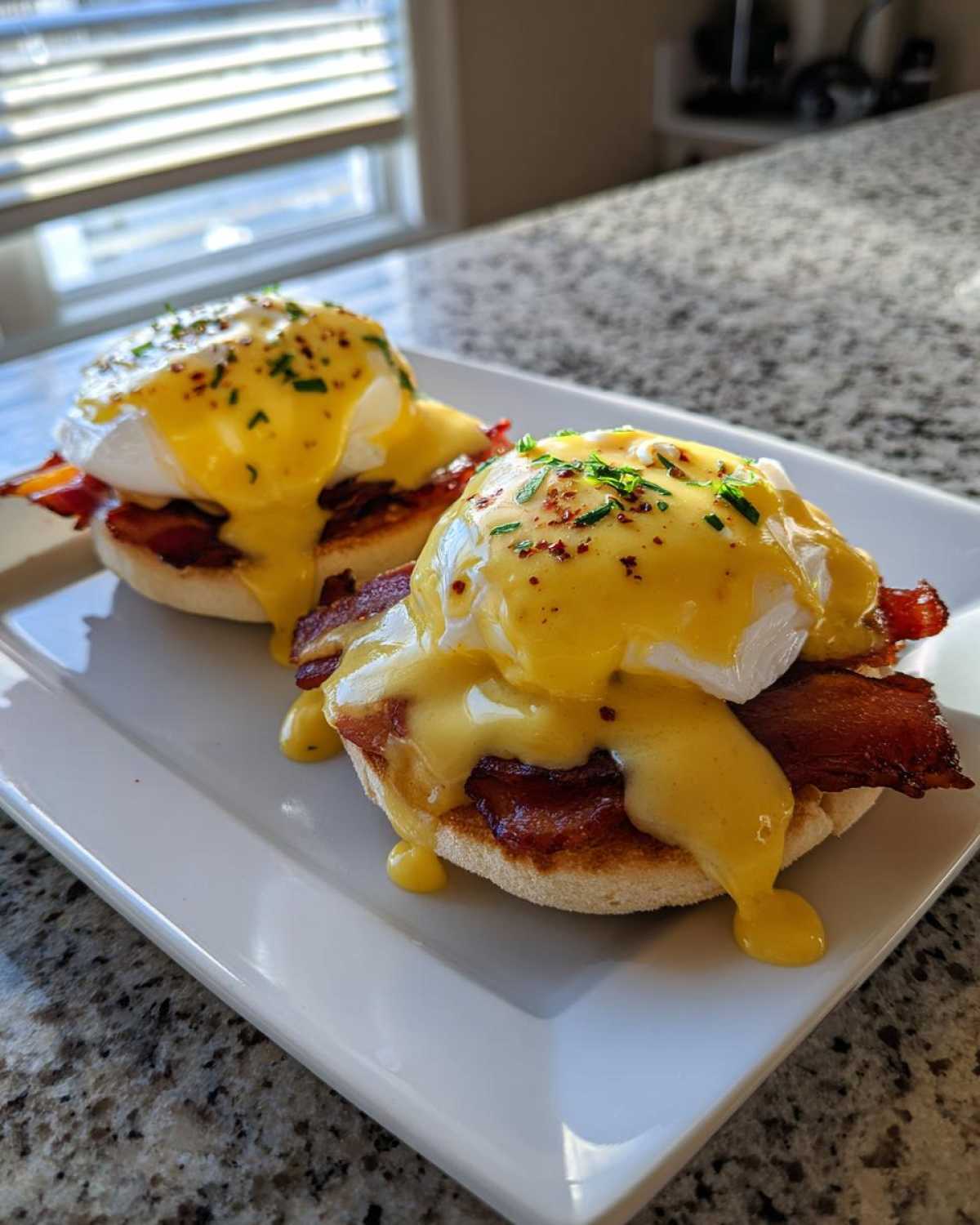 Two servings of delicious eggs benedict featuring poached eggs, bacon, and dripping hollandaise sauce on an English muffin.